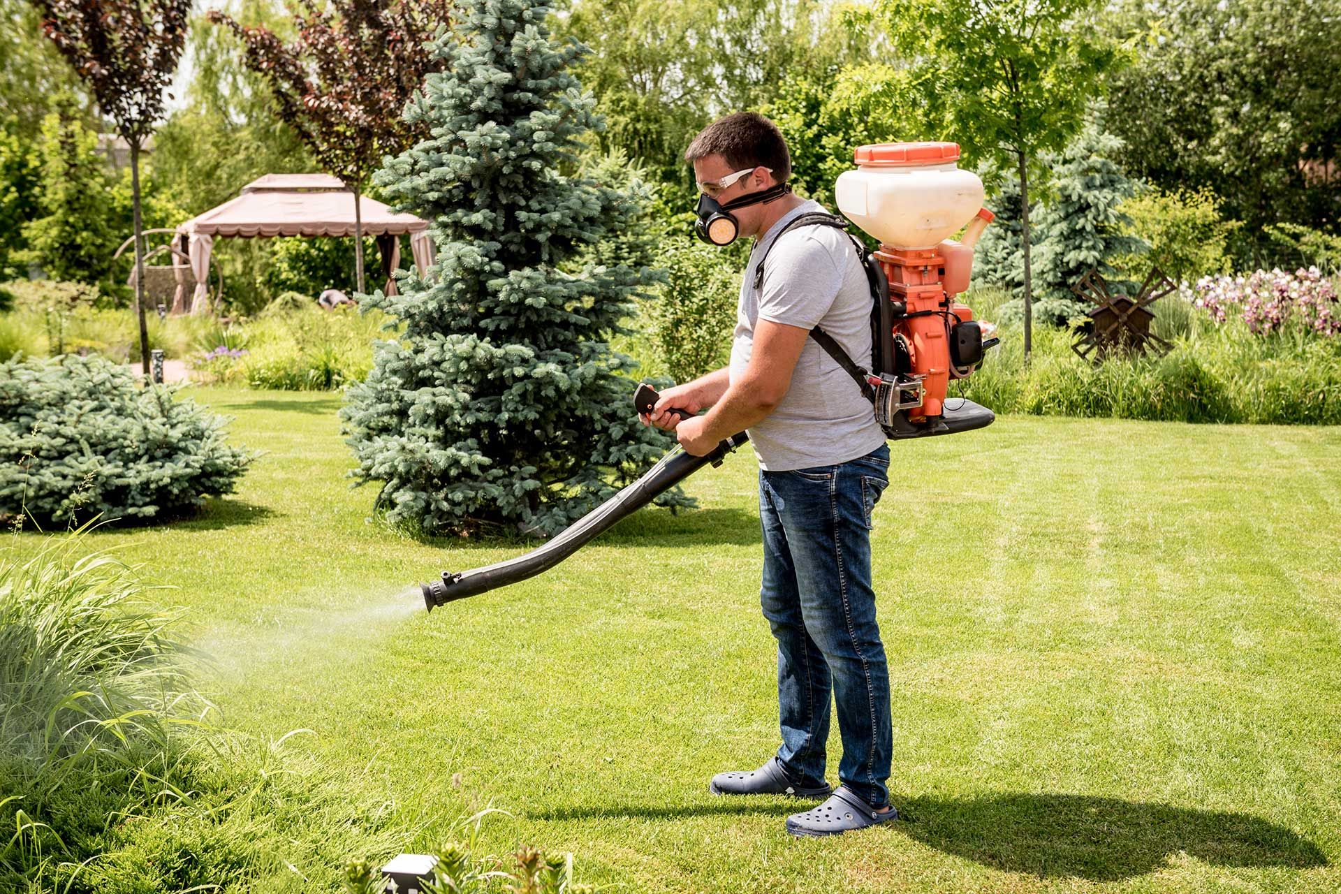 Técnico fumigando un jardín con equipo de aspersión de espalda