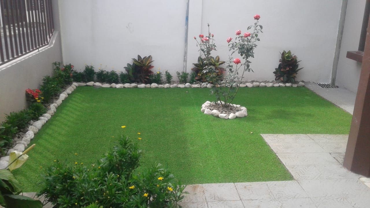 Patio con zacate sintético y borde de piedra decorativa instalado por Green Garden