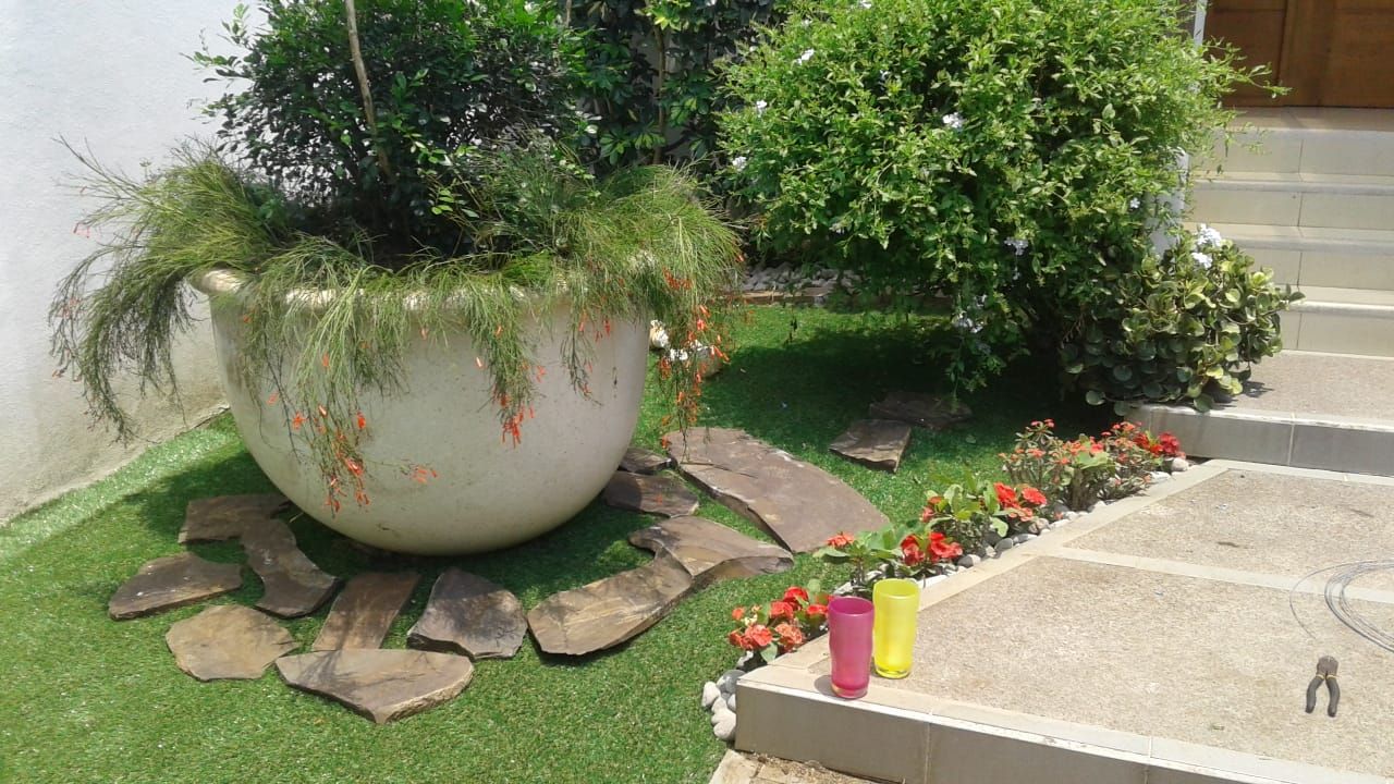Macetero grande con plantas sobre zacate sintético y piedras planas